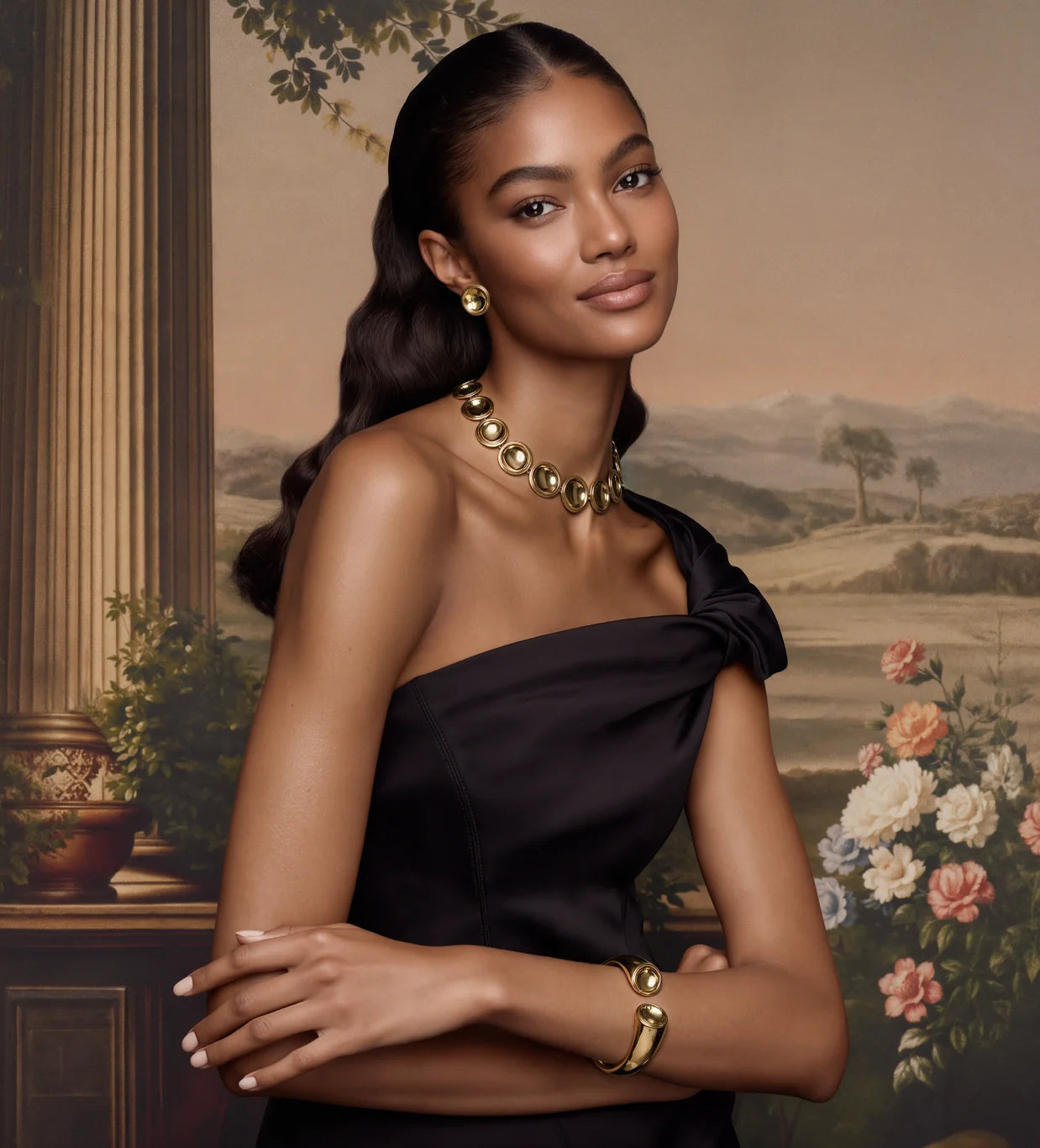 A model in a black dress wearing the Patera Necklace, Earrings and Cuff beside a column and a painted countryside