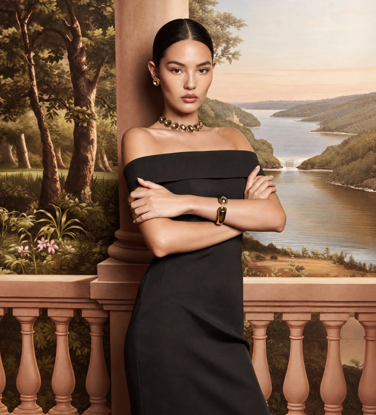 A model in a black dress wearing the Patera Necklace, Earrings and Cuff on a terrace above a painted river valley