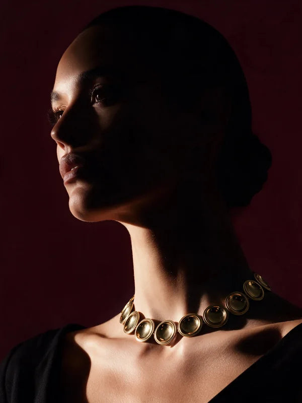 A model in profile wearing the Patera Necklace in gold