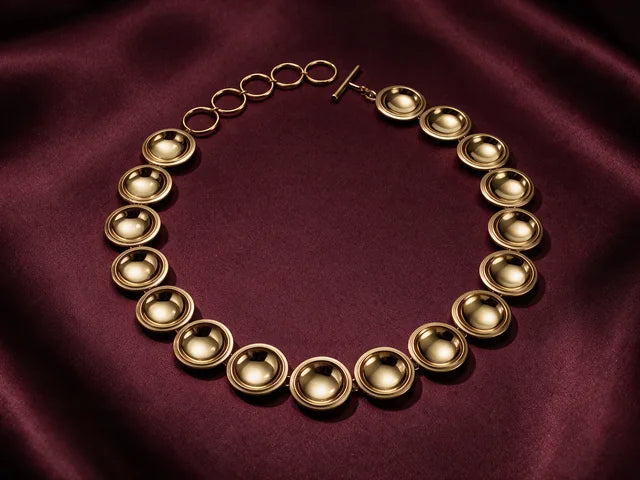 The Patera Necklace in gold laid in a circle on wine cloth