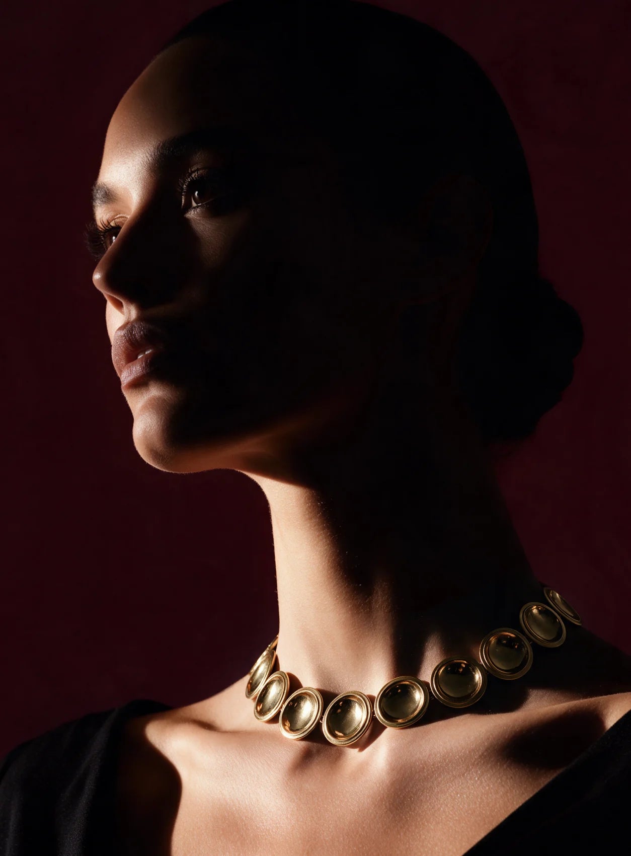 A model in profile wearing the Patera Necklace in gold