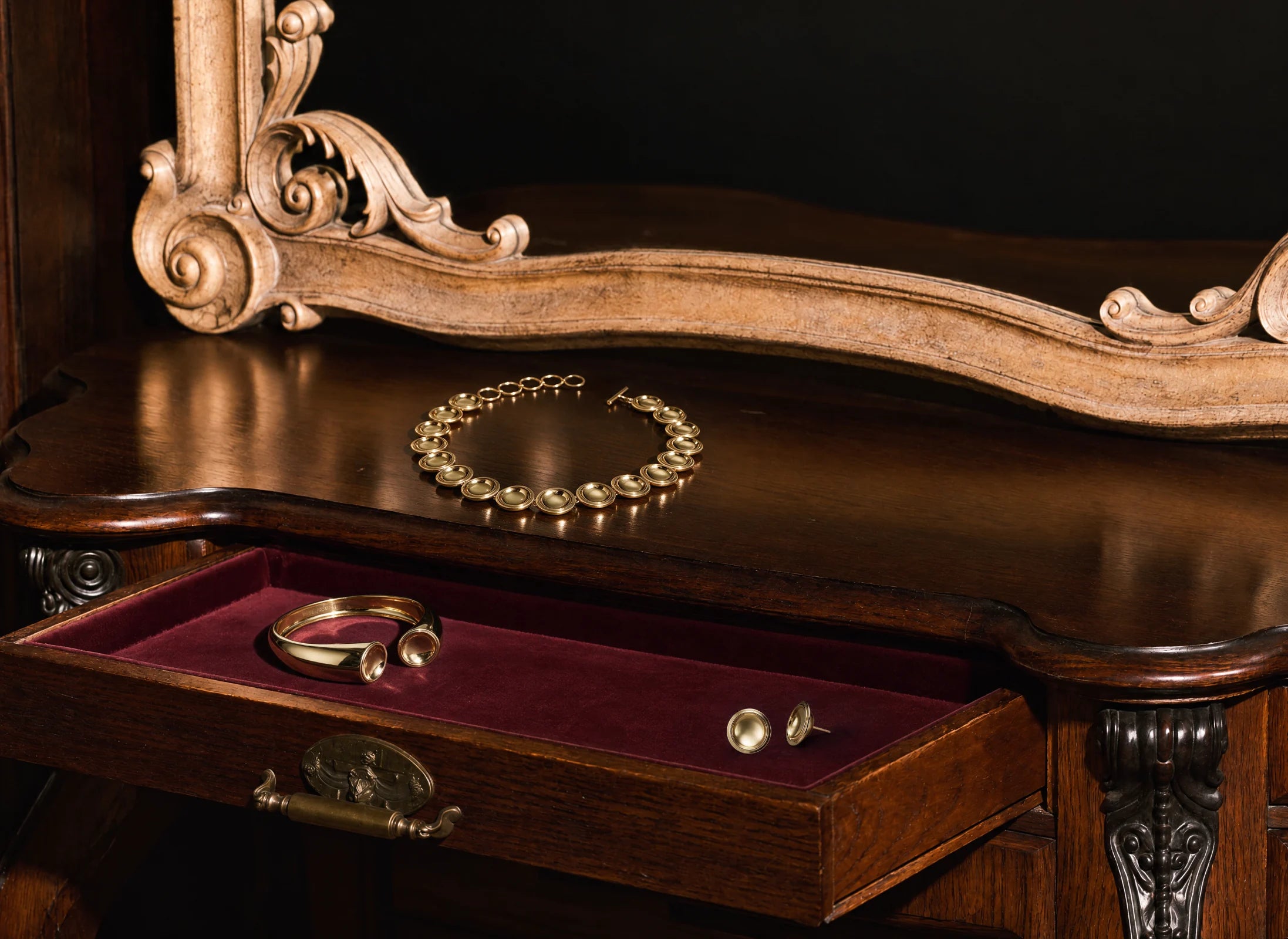 The Patera Necklace, Cuff and Earrings in gold on an antique desk with an open velvet-lined drawer