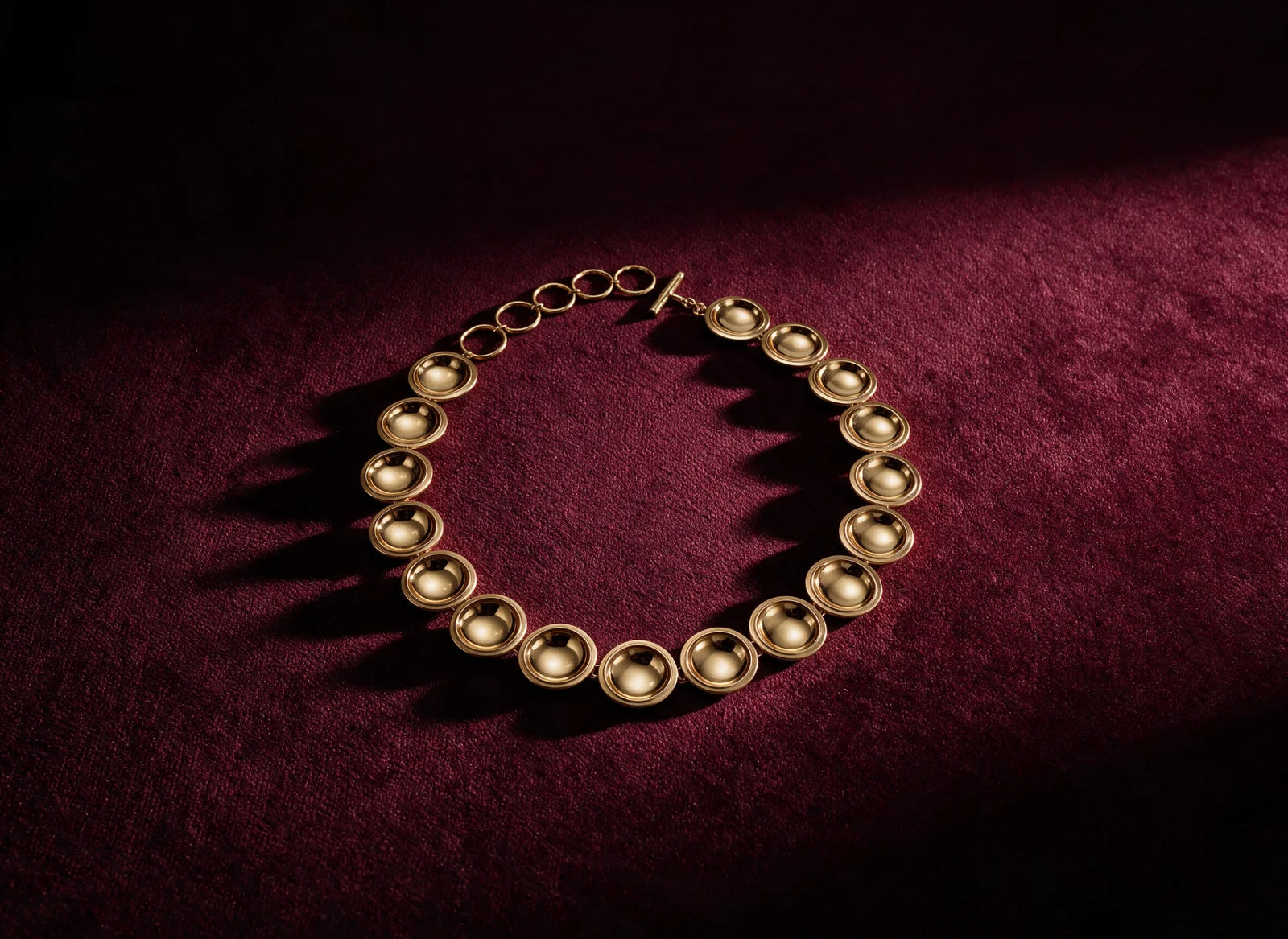 The Patera Necklace in gold laid in a circle on wine cloth
