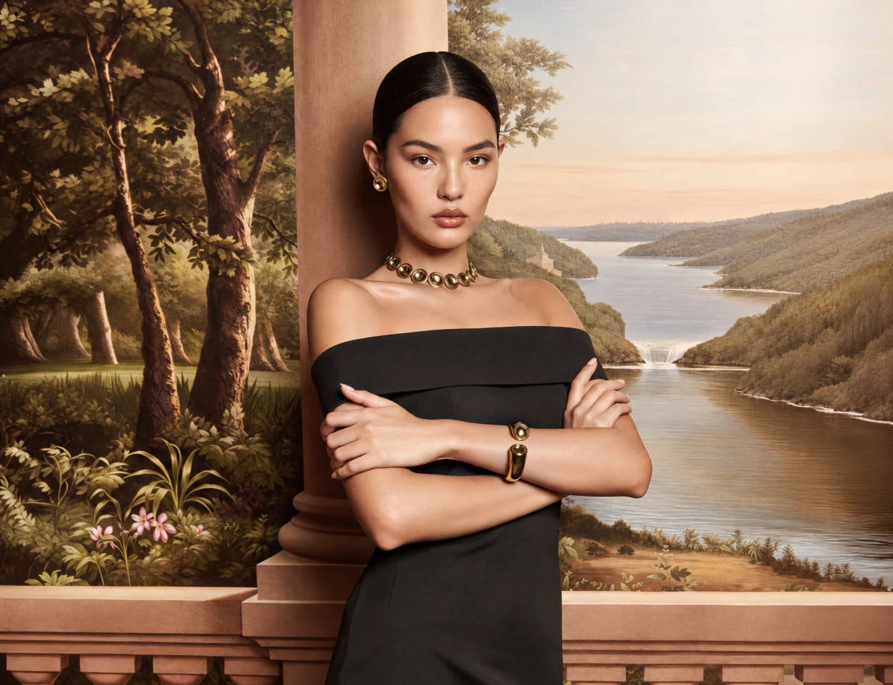 A model in a black dress wearing the Patera Necklace, Earrings and Cuff on a terrace above a painted river valley