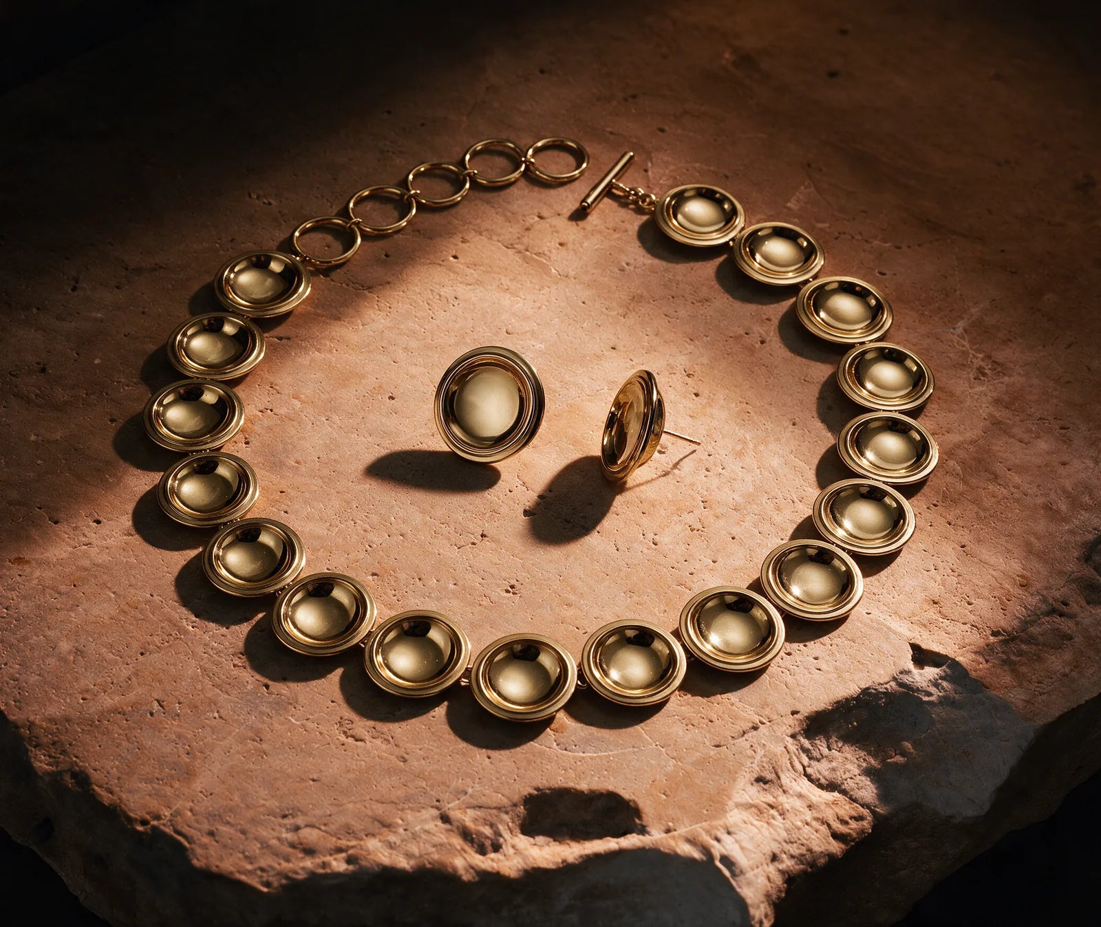 The Patera Necklace and Earrings in gold on sunlit stone